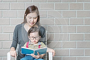 Closeup asian mother is teaching her son to read a book on stone brick wall textured background with copy space