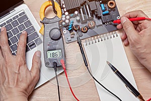 Closeup asian technician man hand measuring electrical voltage of computer mainboard by using digital multimeter.