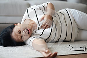 Closeup of Asian woman having heart attack lying on the floor alone at home. Woman touching breast and having chest pain.