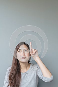 Closeup asian woman holds up one finger point to space with boring face emotion on blurred cement wall textured background with co