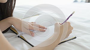 Closeup asian woman relax lying on bed writing book and diary in the bedroom at home
