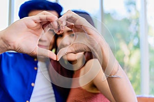 Closeup of asian young couple sitting on couch and looking through a heart shape made with their fingers