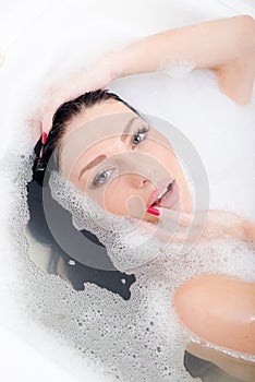 Closeup on attractive beautiful young woman with blue eyes red manicure relaxing sensually lying in spa foam bath