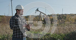 Closeup of attractive engineer man supervising oil pumping near a unit using digital tablet. Engineer in hardhat is