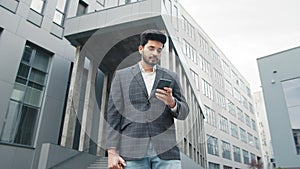 CloseUp of Attractive Young Businessman using Smartphone and Smiles. Texting Messages while standing near Modern Office