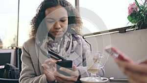 Closeup of Attrcative mixed race woman using credit card shopping online with smartphone in street cafe while have