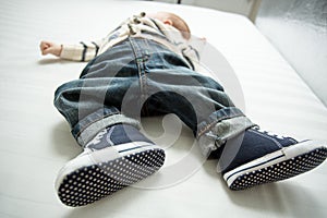 Closeup of baby boy feet in jeans and sneakers lying on bed