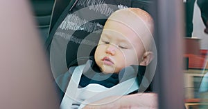 Closeup baby boy sitting in the baby car seat inside of car Father's hands fastening seat belts Picture through the