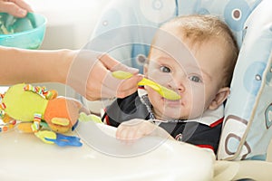 Closeup of baby boy sitting behind table at highchair and eating