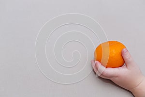 Closeup of baby hands holding tangerine with leaf, healthy eating concept