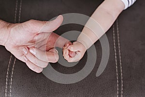 Closeup of a baby holding father`s finger at home. Family and love concept