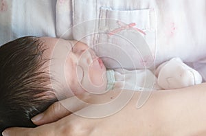 Closeup a baby sleeping comfortably in in the mother`s arms