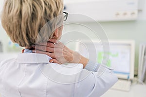 Closeup back view of middle-aged female doctor having neck pain during working on laptop, suffering from injury at