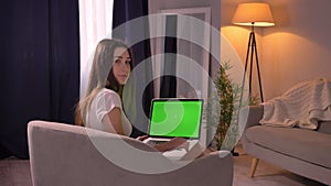 Closeup back view portrait of young caucasian female using the laptop with green chroma screen and turning to camera