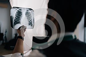 Closeup back view of unrecognizable male doctor examining patient chest x-ray film lungs scan at radiology department in