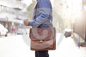 Closeup, bag and man in city, business and commute with travelling, coffee or sunshine with latte. Outdoor, person or