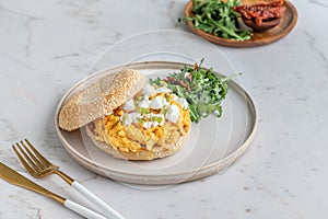 Closeup of a bagel filled with egg served with greens on the side on a white plate