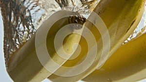 Closeup bananas falling water in light background. Yellow tropical fruits drop