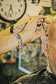 Closeup of barber with bead bracelet trimming older man`s hair with sissors in old fashione barber shop - cut hair falling onto