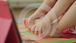 Closeup of a bare feet of a little girl sitting on the floor next to an electronic tablet