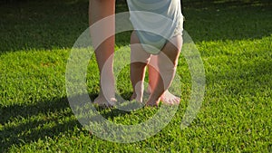Closeup of barefoot baby boy and mother standing on fresh green grass at park. Concept of healthy lifestyle, child