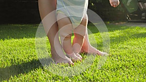 Closeup of barefoot baby with mother standing on fresh green grass lawn at house backyard garden. Concept of healthy