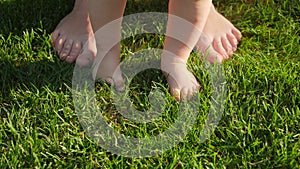 Closeup of barefoot baby standing on fresh green grass with mother. Concept of healthy lifestyle, child development and