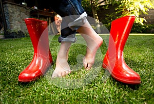 Closeup of barefoot girl standing on grass with red rubber boots