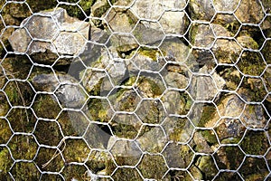 Closeup of a barrier built of small pieces of rock behind a fence of metallic mesh