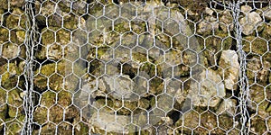 Closeup of a barrier built of small pieces of rock behind a fence of metallic mesh