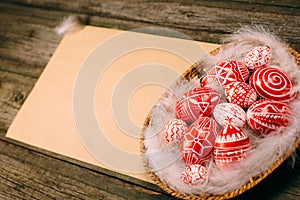 Closeup basket with Easter red eggs on vintage sheet of paper on the right side of wood table. Top view horizontal background