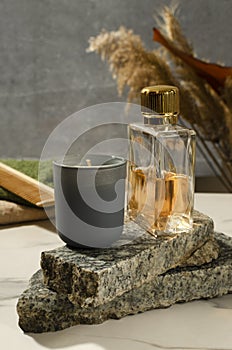 Closeup of bath accessories on the marble shelf against decorative natural leaves and grey wall.Aroma candle, glass bottle of frag