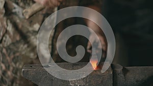 Closeup of bearded young man blacksmith manually forging hot metal on the anvil in smithy with spark fireworks