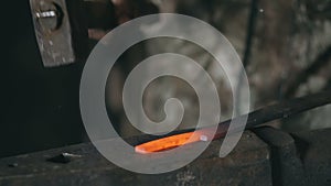 Closeup of bearded young man blacksmith manually forging hot metal on the anvil in smithy with spark fireworks