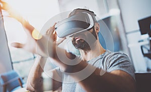 Closeup of bearded young man wearing virtual reality goggles in modern coworking studio. Smartphone using with VR