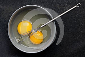 Closeup of beaten eggs in a bowl with a whisk on a black table