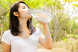 Beautiful Asian woman drinking fresh water in bottle outdoors with nature background