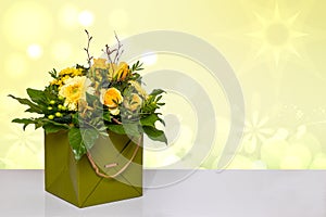 Closeup of a beautiful bouquet of yellow flowers in a decorative green gift box on a bright table over a abstract spring