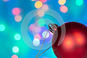 Closeup of a beautiful Christmas tree decoration toy red ball on the background of blurry lights garland