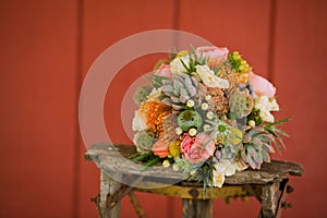 Closeup of beautiful colorful bouquet of flowers of bride on old wooden chair on red wall background