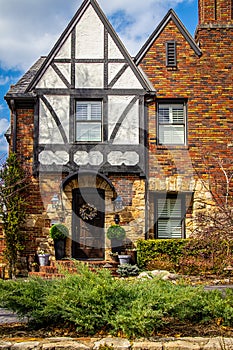 Closeup of beautiful entranceway of vintage brick and rock house with half timbered tudor gable with beautiful landscaping and