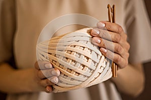 Closeup beautiful female hands hold hank reel of beige ribbon yarn and wooden crochet needles