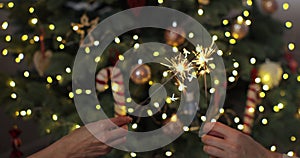 Closeup of beautiful female and man hands holding two stick of holiday sparkler burning isolated at blurry Christmas
