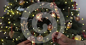 Closeup of beautiful female and man hands holding two stick of holiday sparkler burning isolated at blurry Christmas