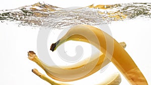 Closeup beautiful image of bananas falling in clear water against white background, Lots of air flaoting air bubbles and
