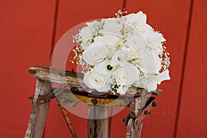 Closeup of a beautiful white bouquet of flowers of bride on old wooden chair on red wall background