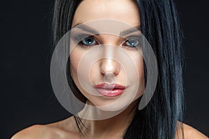 Closeup of beautiful woman face with beauty makeup and long brunette hair looking at camera isolated on black background