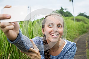 Closeup of beautiful woman taking a selfie on smart phone outdoors in summer. Young woman photographing herself smiling.