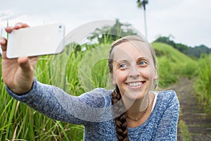 Closeup of beautiful woman taking a selfie on smart phone outdoors in summer. Young woman photographing herself smiling.