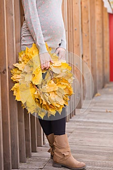 Closeup of beautiful yellow maple wreath in girl`s hands. Pregnant woman holding autumn leaves. Fall